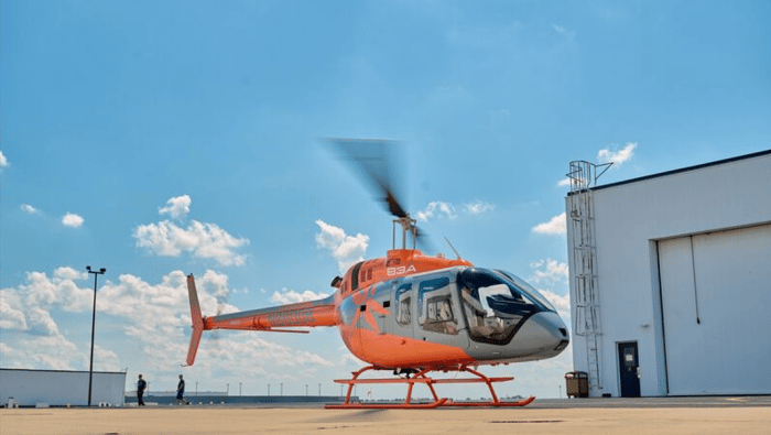 Orange and grey Bell 505 helicopter outside hangar 
