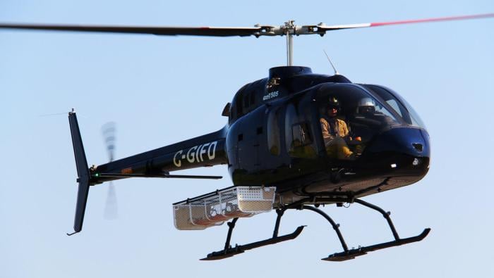 A Bell 505 helicopter in the air with a Dart utility basket attached to the side