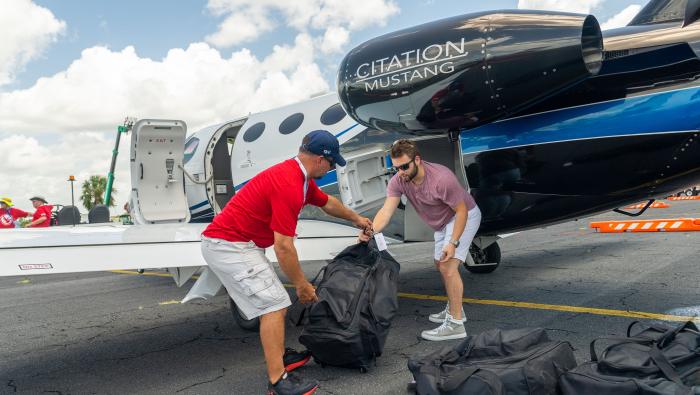 Two individuals load a bag into the cargo hold of a small business jet