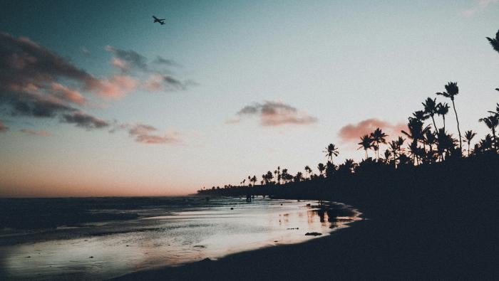 an airplane in the sky at dusk over the beach