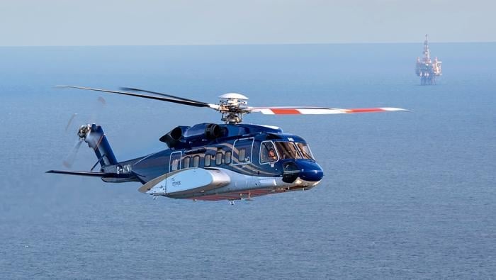 A helicopter flies over the ocean with a rig in the far background