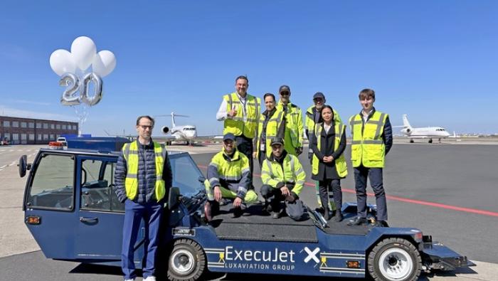 ExecuJet crew standing on ground handling vehicle, jets on apron in background 