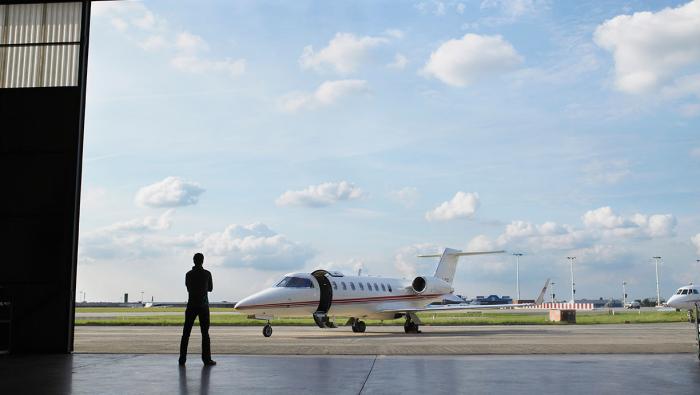 Nimbl image silhouette of a person standing in a hangar door looking at an aircraft on the ramp