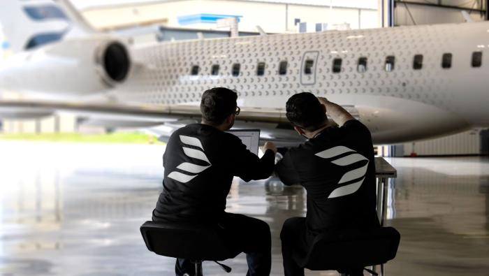 Two engineers sitting at screen in front of Bombardier biz-jet 