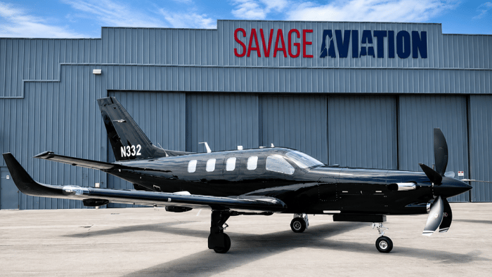 A Daher TBM 980 is parked on a ramp in front of Savage Aviation hangar