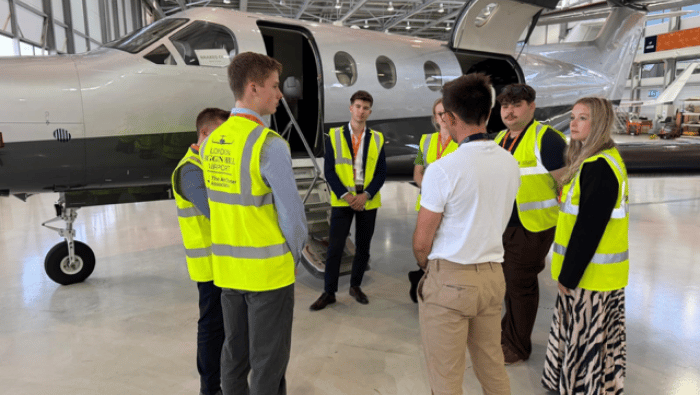 Students standing in hangar in yellow hi-viz jackets 