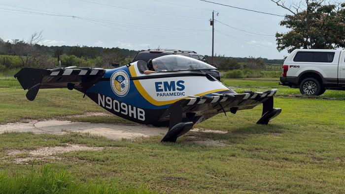 A Pivotal BlackFly in Hyde County Emergency Services livery, N909HB, sits on grass beside a rural driveway. 