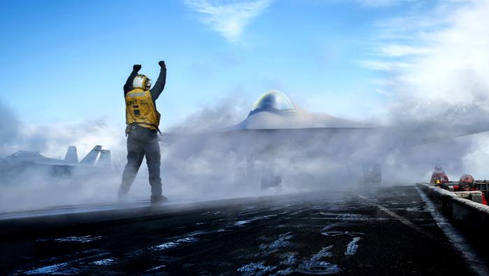 Aircraft carrier deck marshaller with aircraft shrouded in smoke 