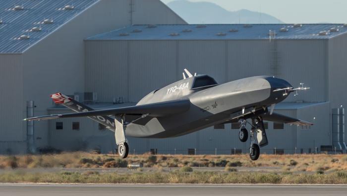 Uncrewed aircraft getting airborne from runway, hangar in background