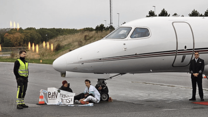 Three activists sitting on tarmac beside jet 