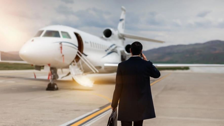A man walks across an airport ramp to a corporate jet, briefcase in one hand, talking on the phone