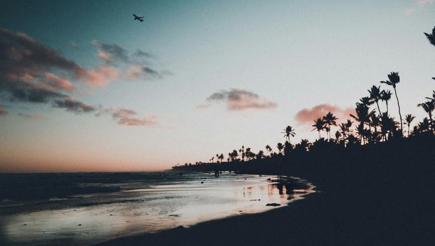 an airplane in the sky at dusk over the beach
