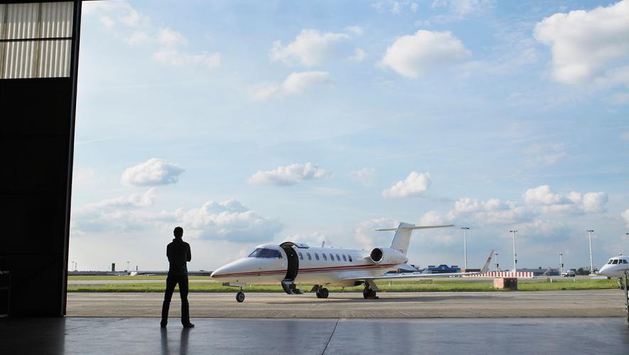 Nimbl image silhouette of a person standing in a hangar door looking at an aircraft on the ramp