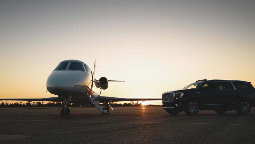 A jet parked on an airport ramp at dusk with an SUV parked near its wing