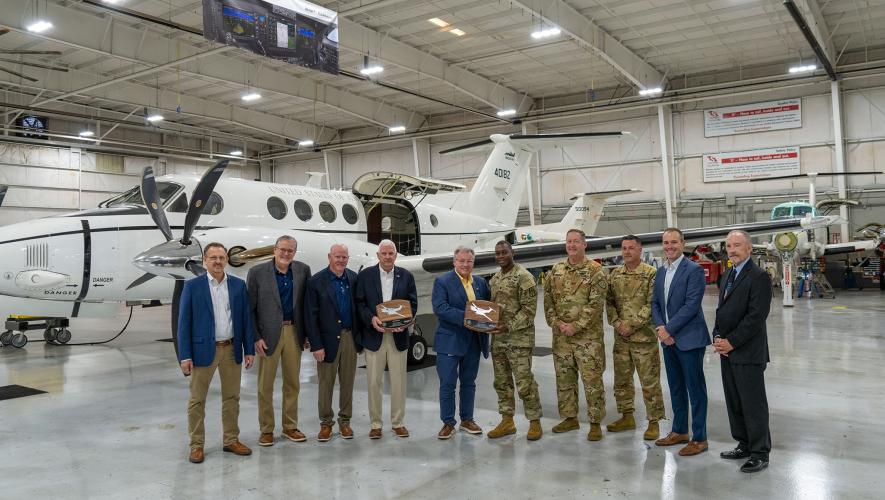 Army and industry officials stand with a U.S. Army C-12 Huron in a hangar.