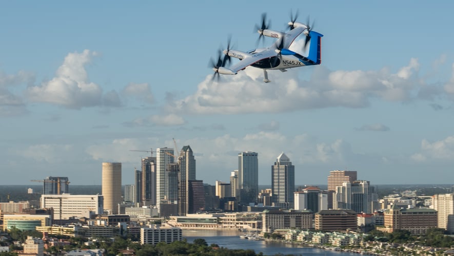 Joby’s white and blue S4 air taxi flying above the downtown Tampa skyline.