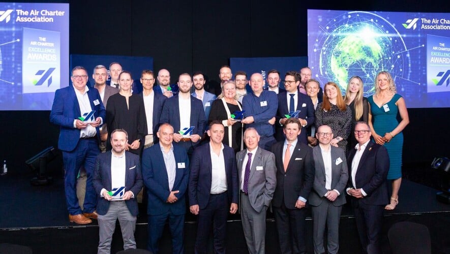 Group of prizewinners smiling on stage holding glass trophies 