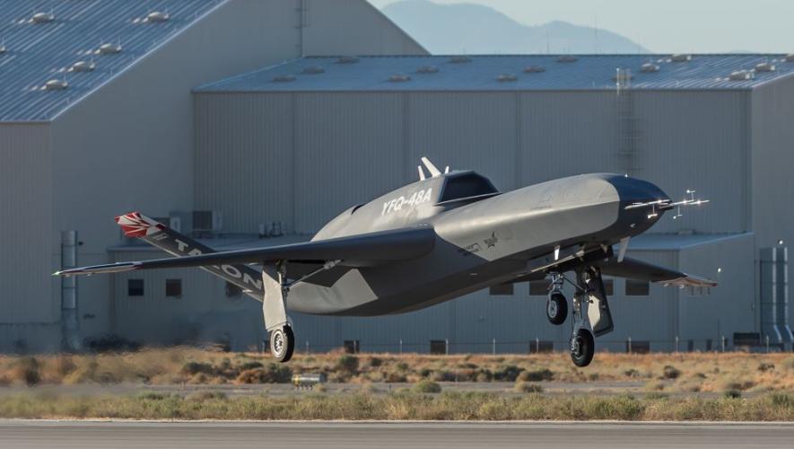 Uncrewed aircraft getting airborne from runway, hangar in background