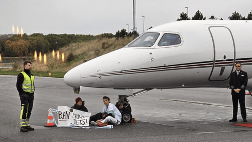 Three activists sitting on tarmac beside jet 