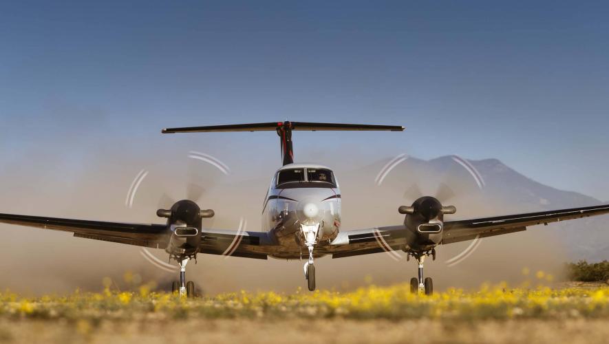 Front view of Beechcraft King Air 360 on takeoff from grass strip backdropped with mountains