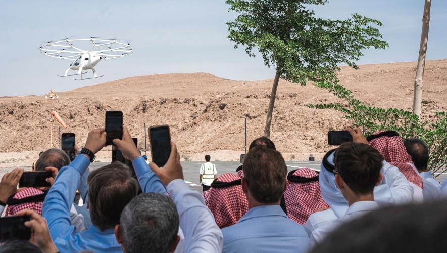 A crowd watches as the VoloCity aircraft flies over the desert of Saudi Arabia