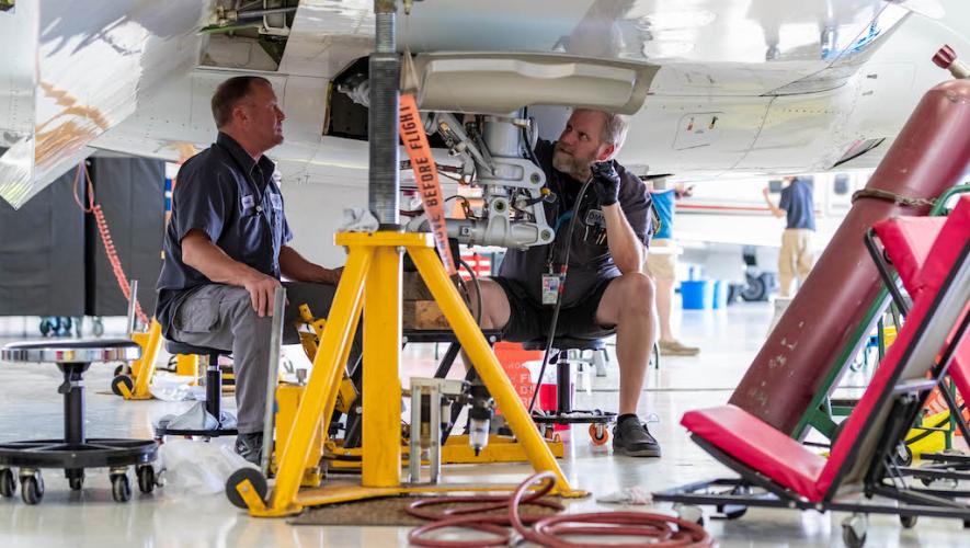 Omni Aircraft Maintenance technicians at work underneath aircraft wing