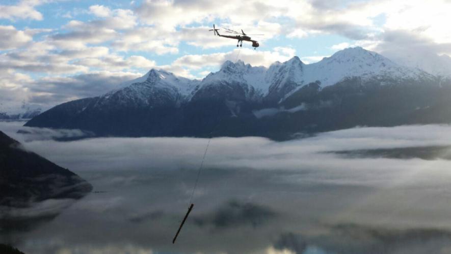 Erickson S-64E Skycrane in flight near mountains hauling log on hoist