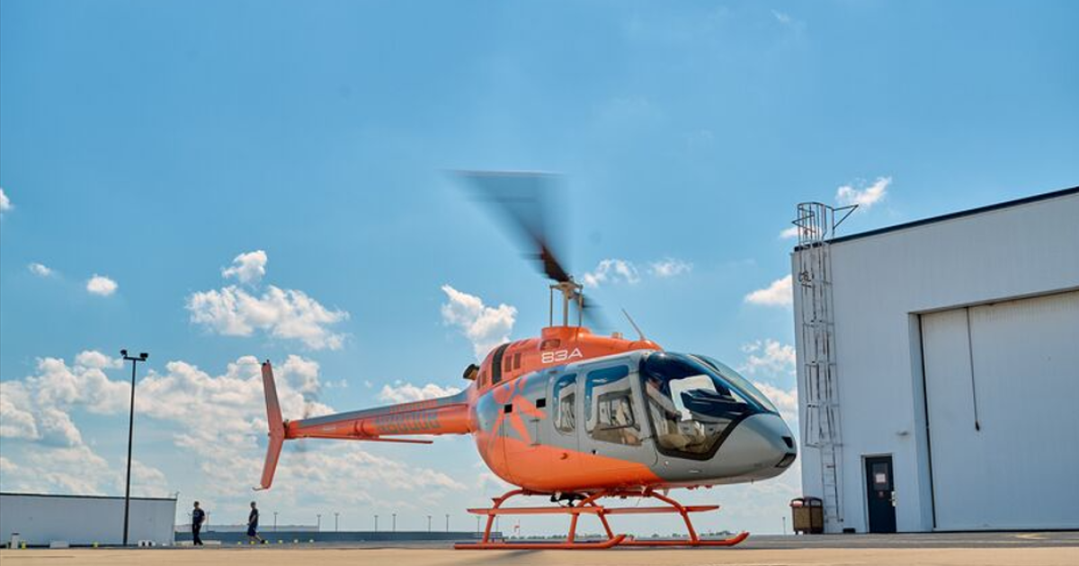 Orange and grey Bell 505 helicopter outside hangar 