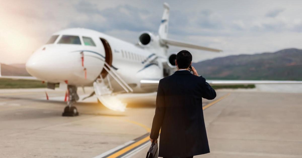 A man walks across an airport ramp to a corporate jet, briefcase in one hand, talking on the phone
