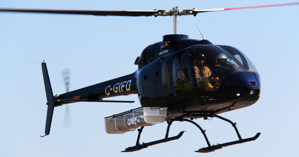 A Bell 505 helicopter in the air with a Dart utility basket attached to the side