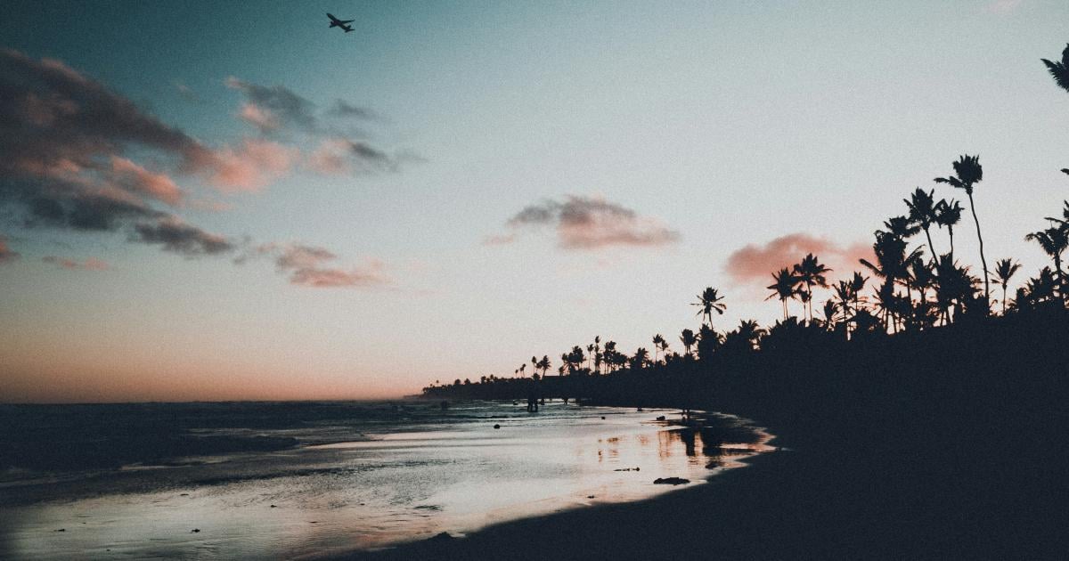 an airplane in the sky at dusk over the beach