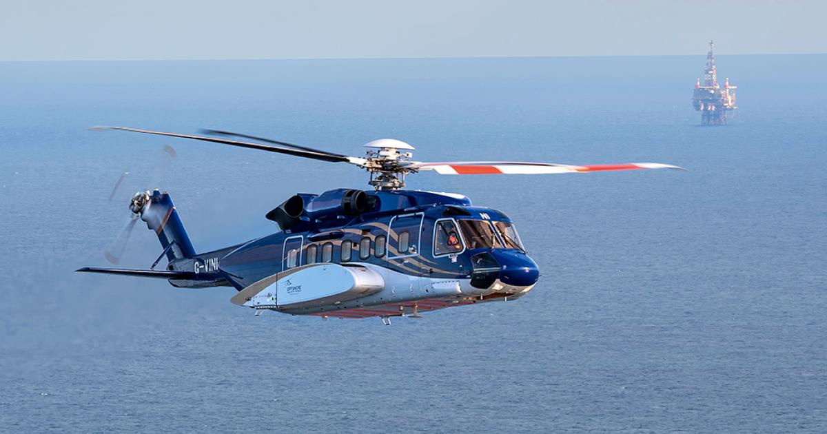 A helicopter flies over the ocean with a rig in the far background