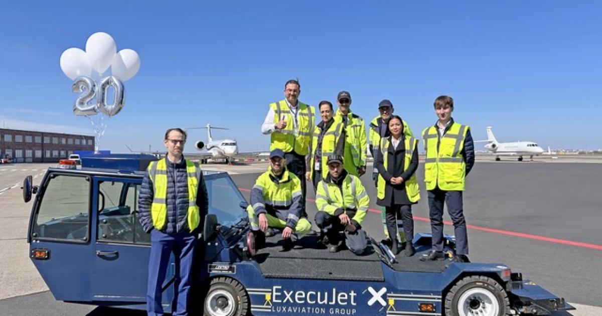 ExecuJet crew standing on ground handling vehicle, jets on apron in background 