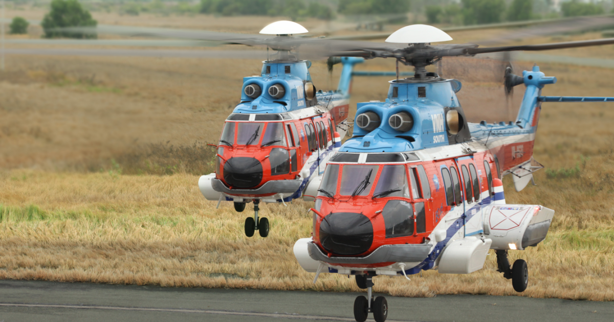 Two VNH-painted orange and blue H225s hovering above tarmac 