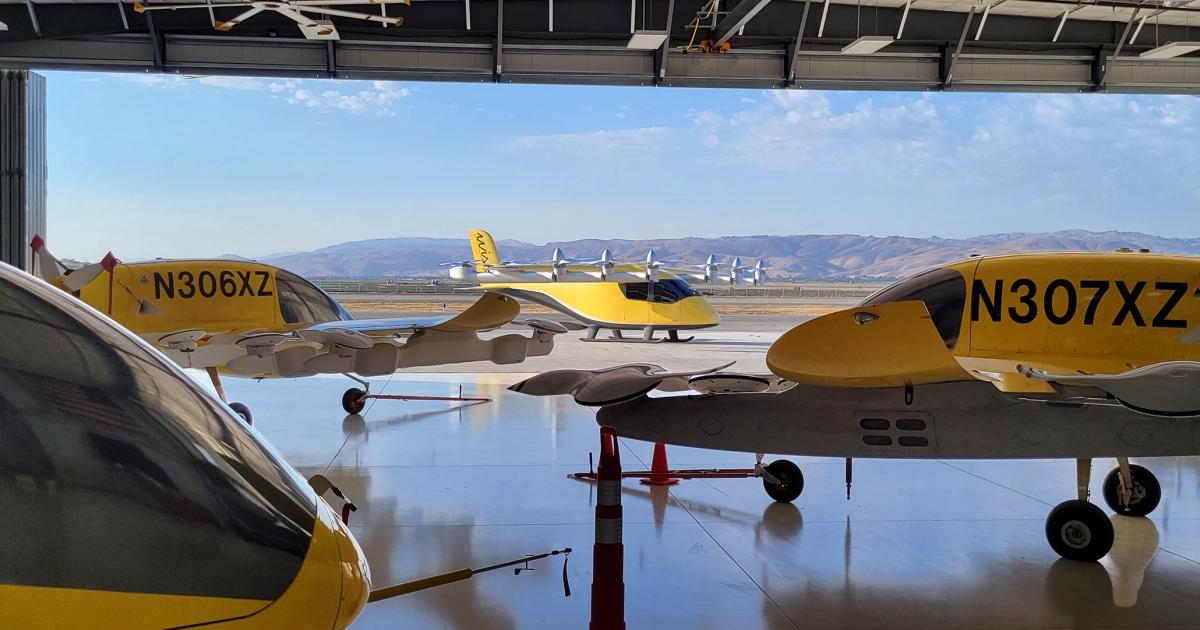 Wisk Aero's fifth-generation Cora prototypes sit in the company's hangar in Hollister, California, as a sixth-generation aircraft crosses the apron outside.
