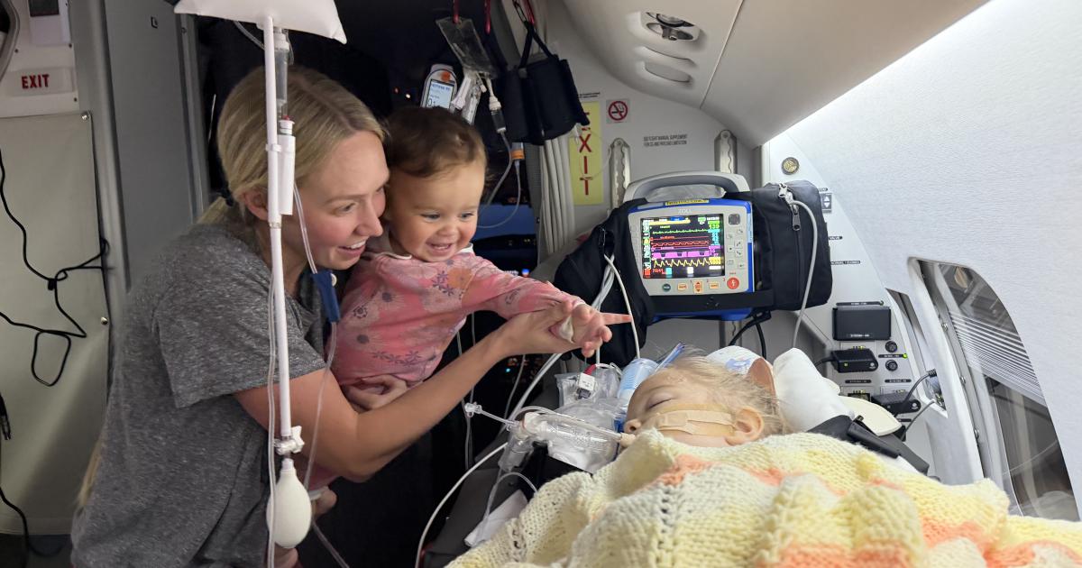 A toddler patient on a bed in a medevac business jet, with a woman and baby visiting with her and smiling