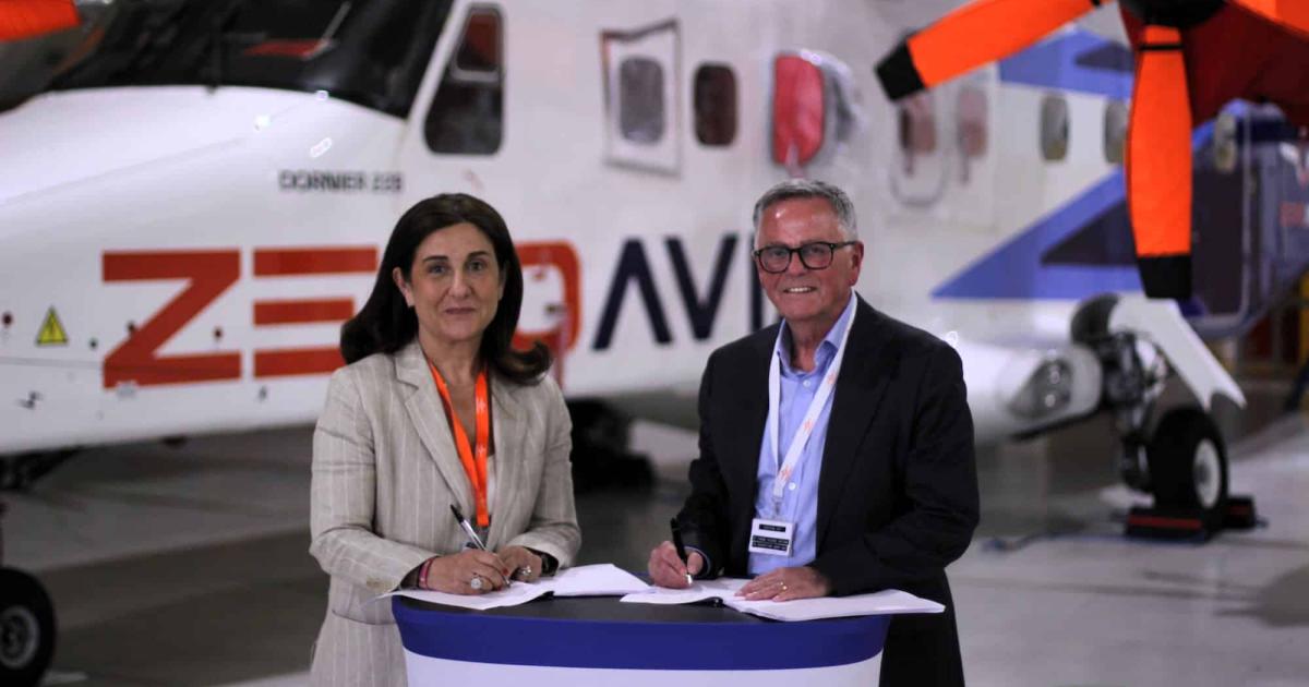 Two people signing at lectern with Dornier 228 in background of hangar 