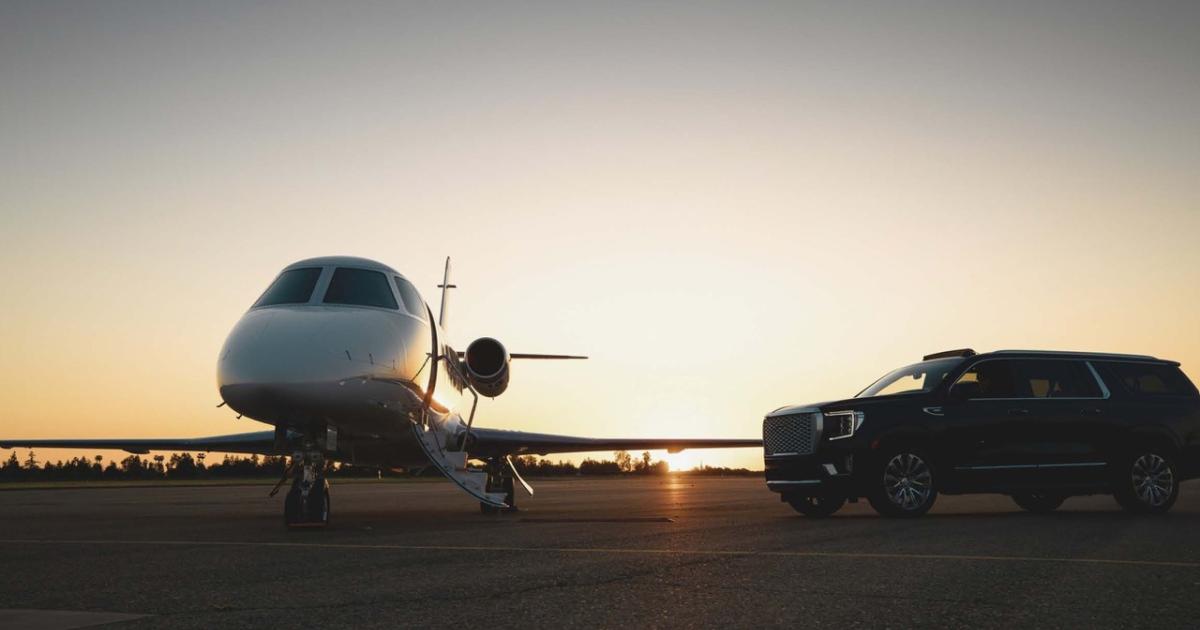 A jet parked on an airport ramp at dusk with an SUV parked near its wing