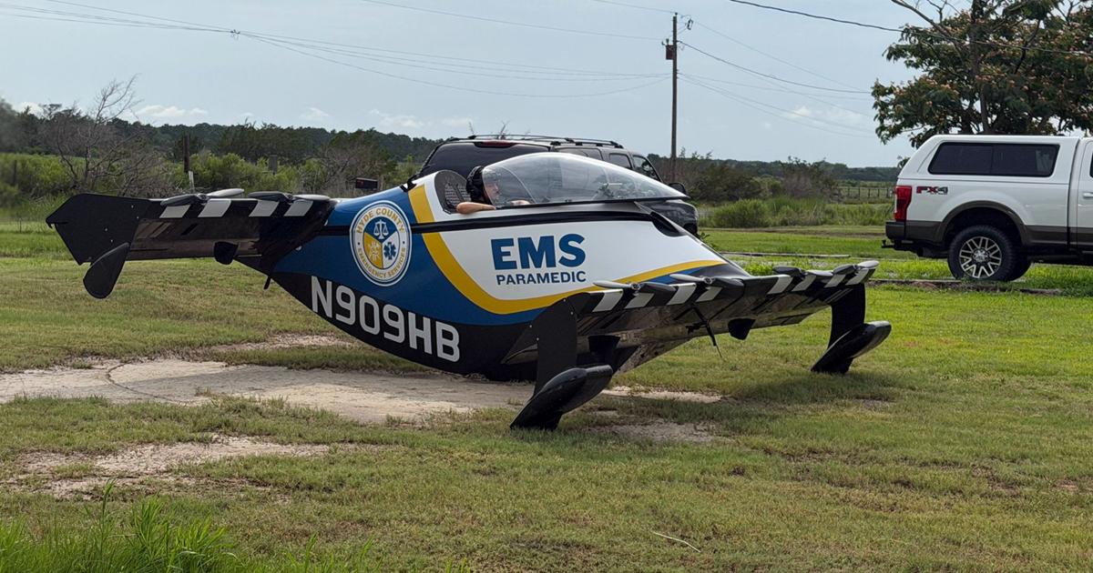 A Pivotal BlackFly in Hyde County Emergency Services livery, N909HB, sits on grass beside a rural driveway. 