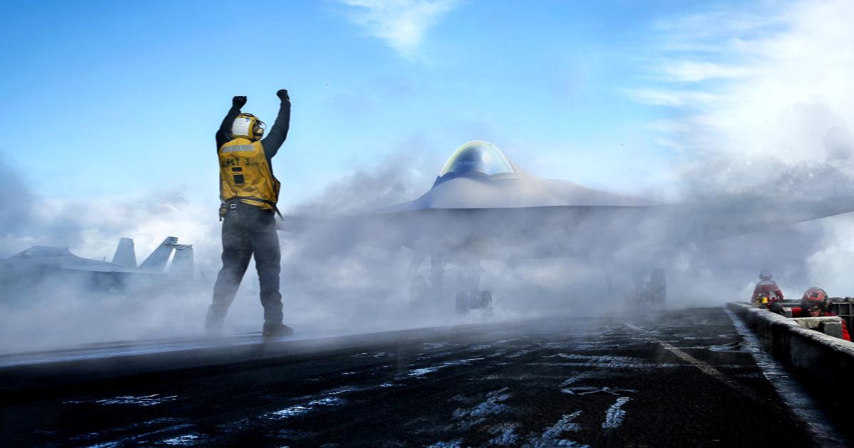 Aircraft carrier deck marshaller with aircraft shrouded in smoke 