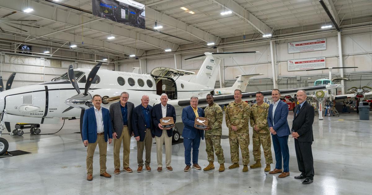 Army and industry officials stand with a U.S. Army C-12 Huron in a hangar.