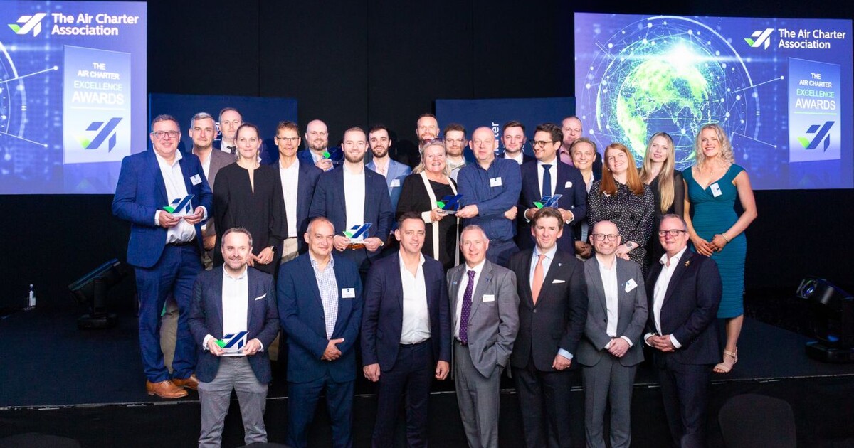 Group of prizewinners smiling on stage holding glass trophies 
