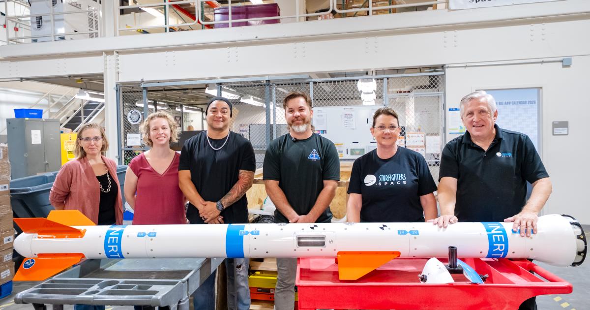 Starfighters Space CEO Tim Franta (right) stands with an inert Wind Tunnel in the Sky carrier on October 16 in a receiving area next to Bionetics’ payload processing lab in Florida.