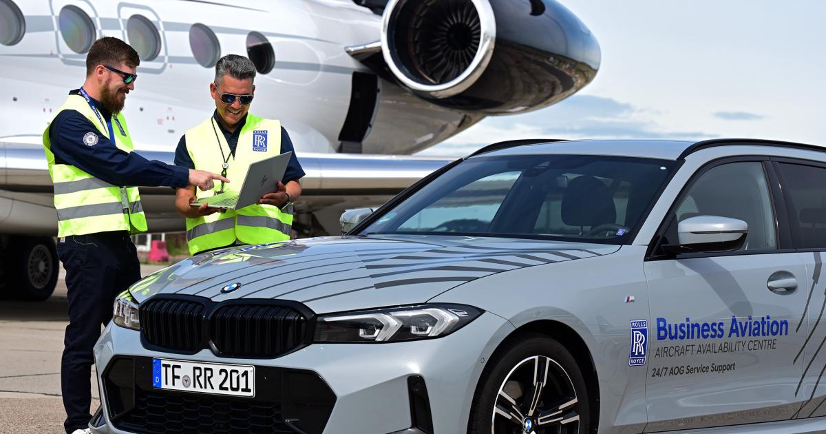 Two Rolls-Royce staff in high-visibility vests look at a laptop beside a business jet and a Rolls-Royce AOG support car.