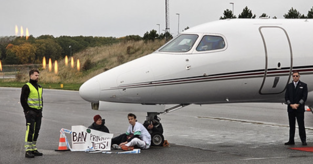 Three activists sitting on tarmac beside jet
