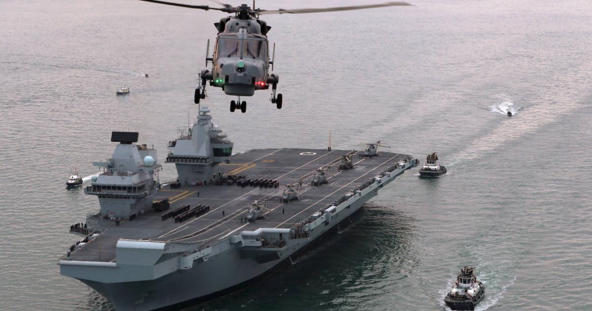 A Wildcat helicopter departs HMS Queen Elizabeth as it prepares to enter Portsmouth harbor. Five Merlin helicopters are parked on the deck. (Photo: UK MoD Crown)
