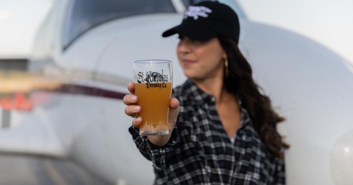 model holding glass of St. Nicholas Brewing Company beer in front of business aircraft parked on airport at Southern Illinois Airport