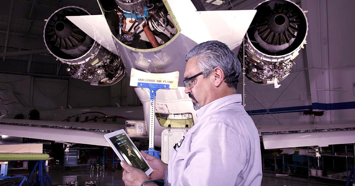 Aviation maintenance technician views iPad underneath tail of business jet