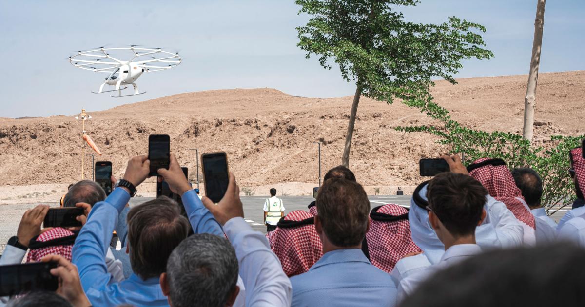 A crowd watches as the VoloCity aircraft flies over the desert of Saudi Arabia